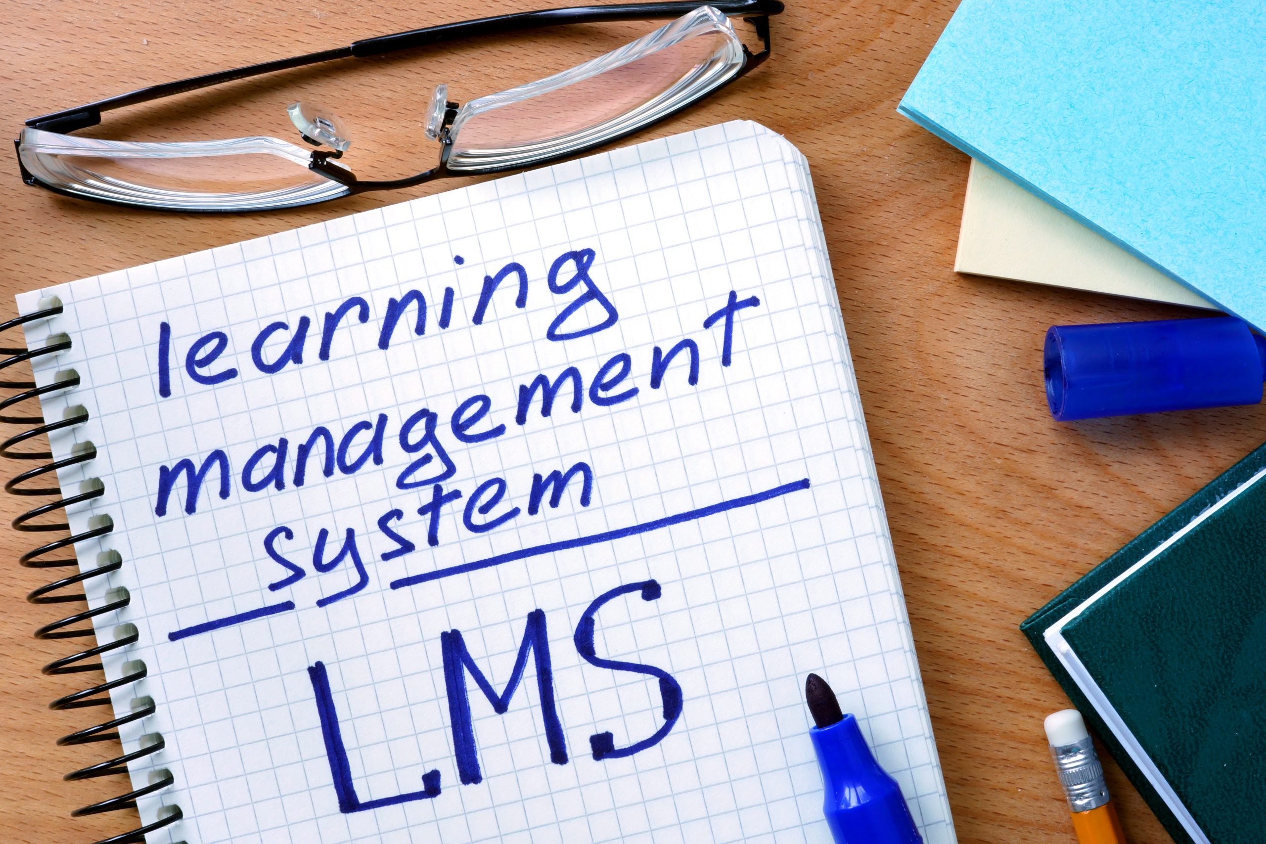 Notepad with learning management system LMS on office wooden table.